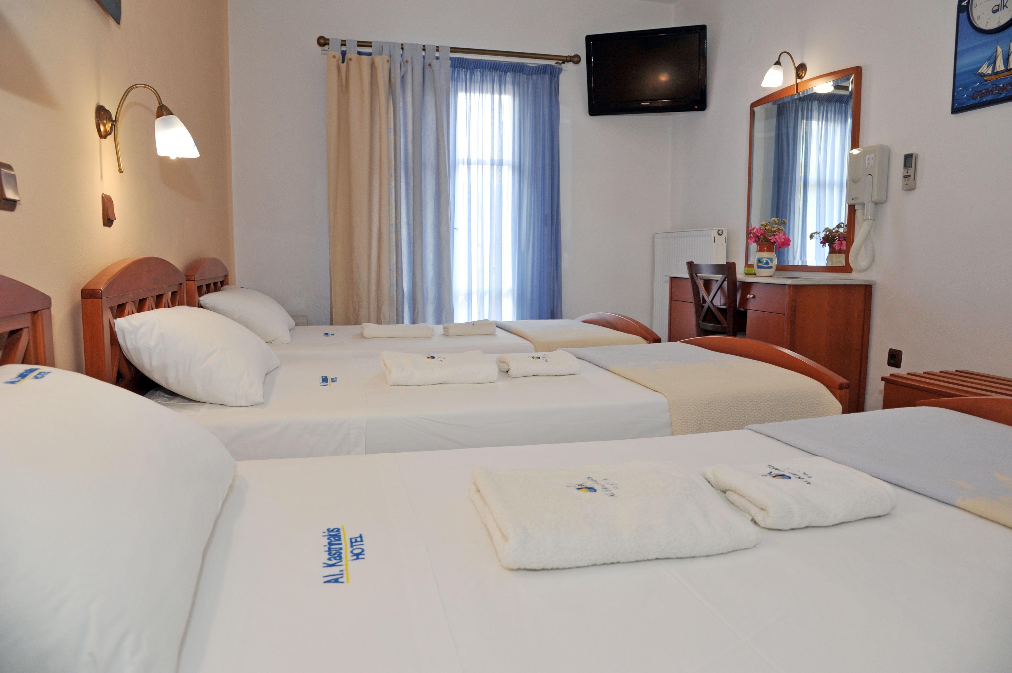 Une chambre d’hôtel avec trois lits, une télévision, un miroir et une fenêtre avec des rideaux.
