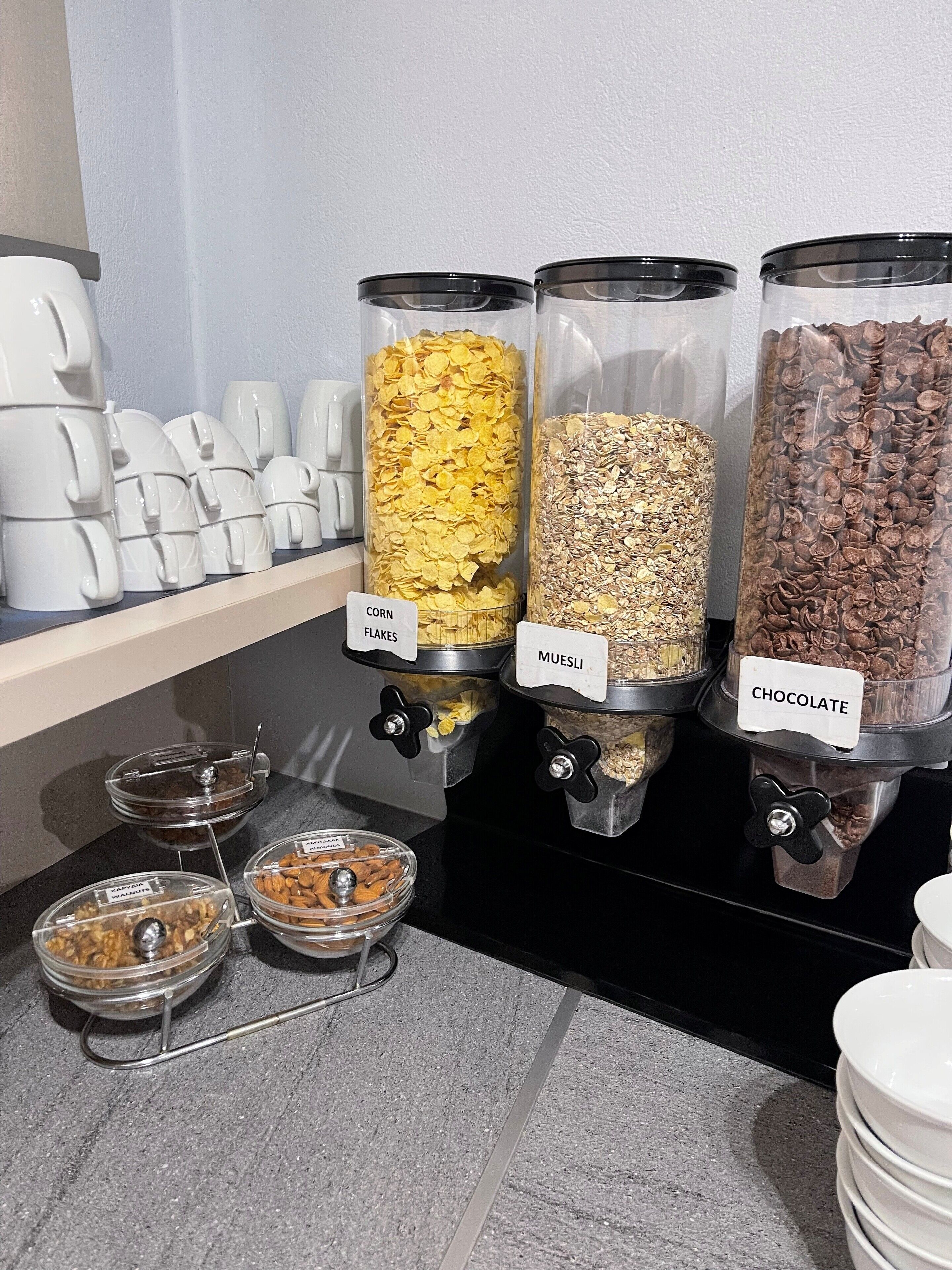 Un buffet où les clients peuvent se servir eux-mêmes, avec des distributeurs étiquetés contenant des céréales de maïs, du muesli et des pépites de chocolat.