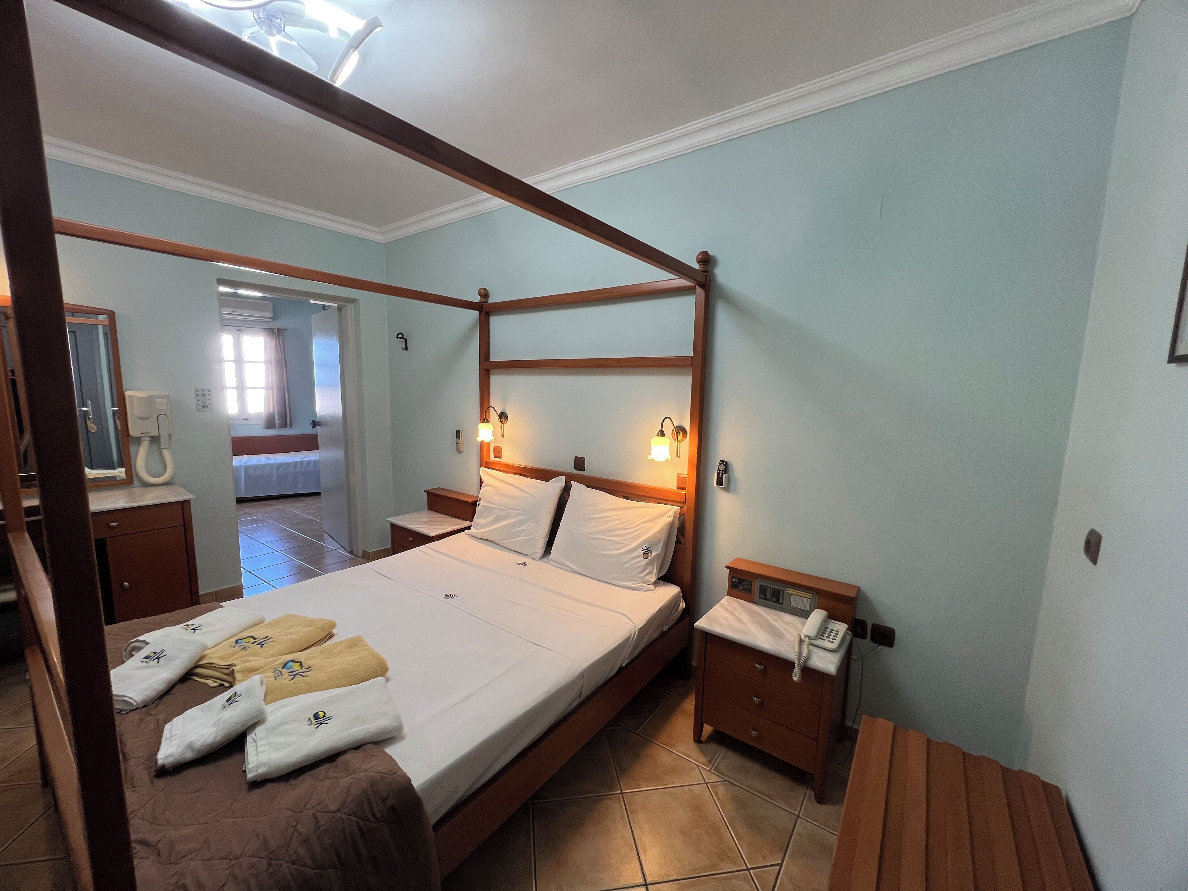 A four-poster bed with a wooden frame, a bedside table with a lamp, and a telephone.