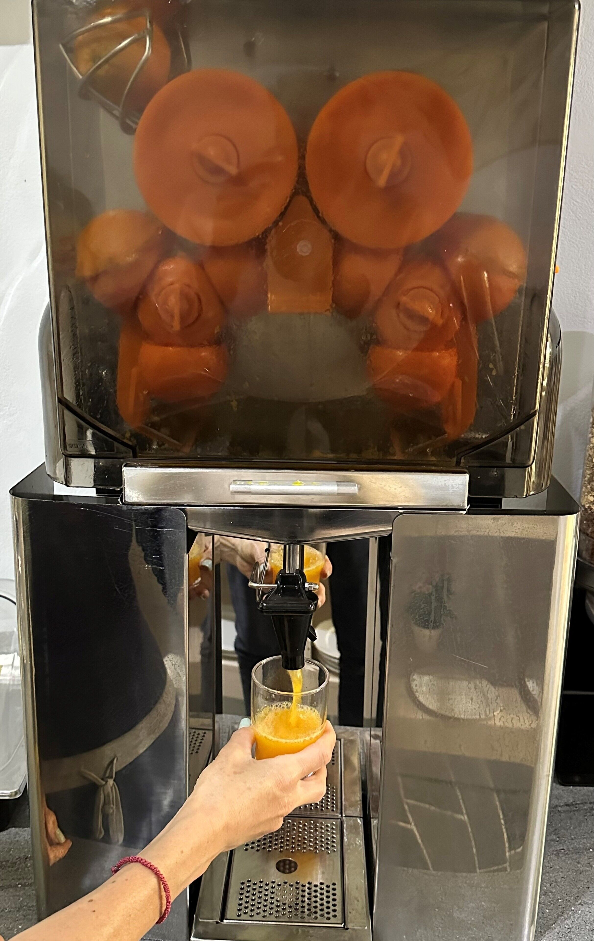 Mão segurando um copo recebendo suco de laranja de um espremedor industrial.