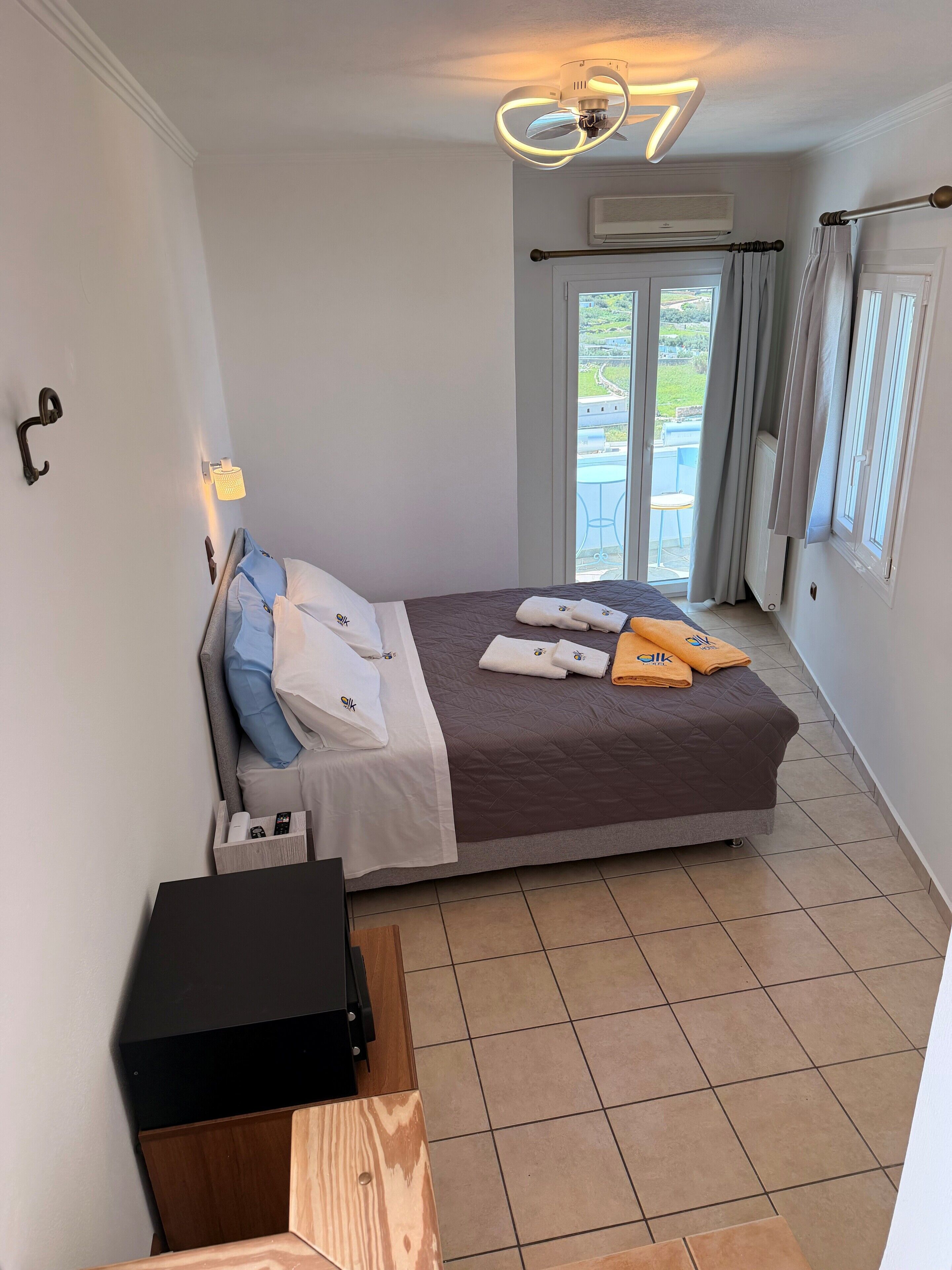 Un dormitorio ordenado con cama, mesita de noche y vistas al exterior.