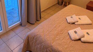 A hotel room with a bed, a TV, a mirror, a window with curtains, and a view of buildings outside.