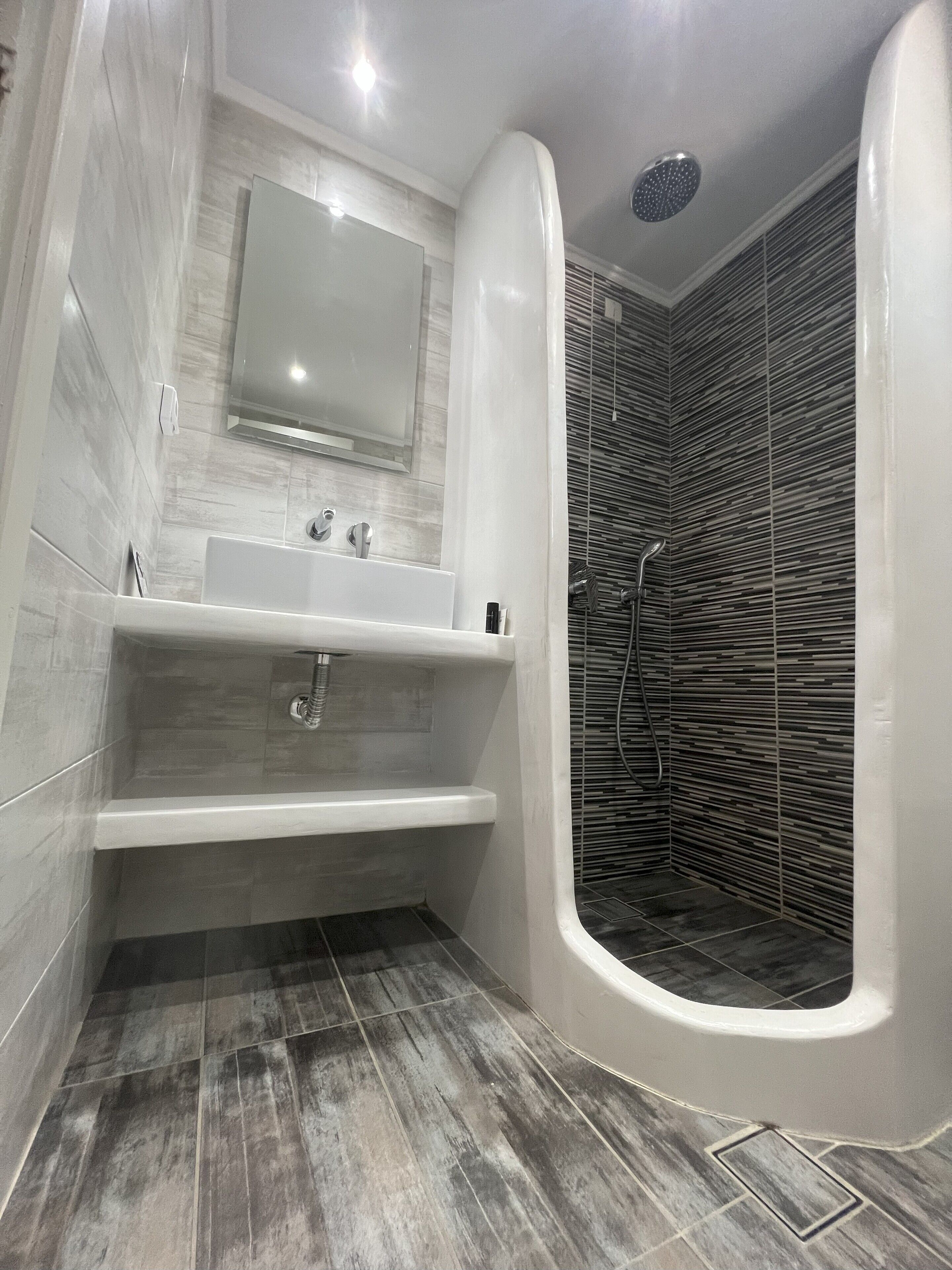 A modern bathroom with a freestanding bathtub, a vanity with a mirror, and a shower area with a unique textured wall.