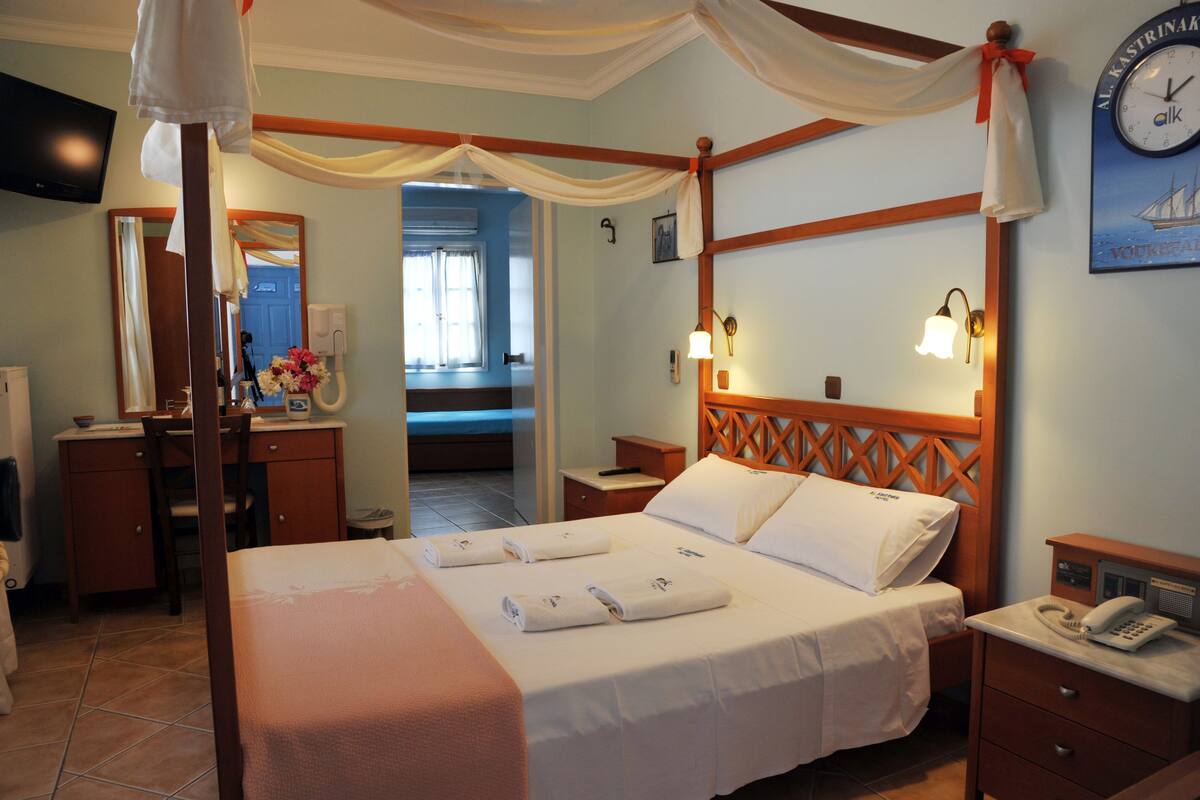 Ein Hotelzimmer mit Himmelbett, Holz-Kopfteil, Nachttisch mit Lampe, Telefon und Wanduhr.