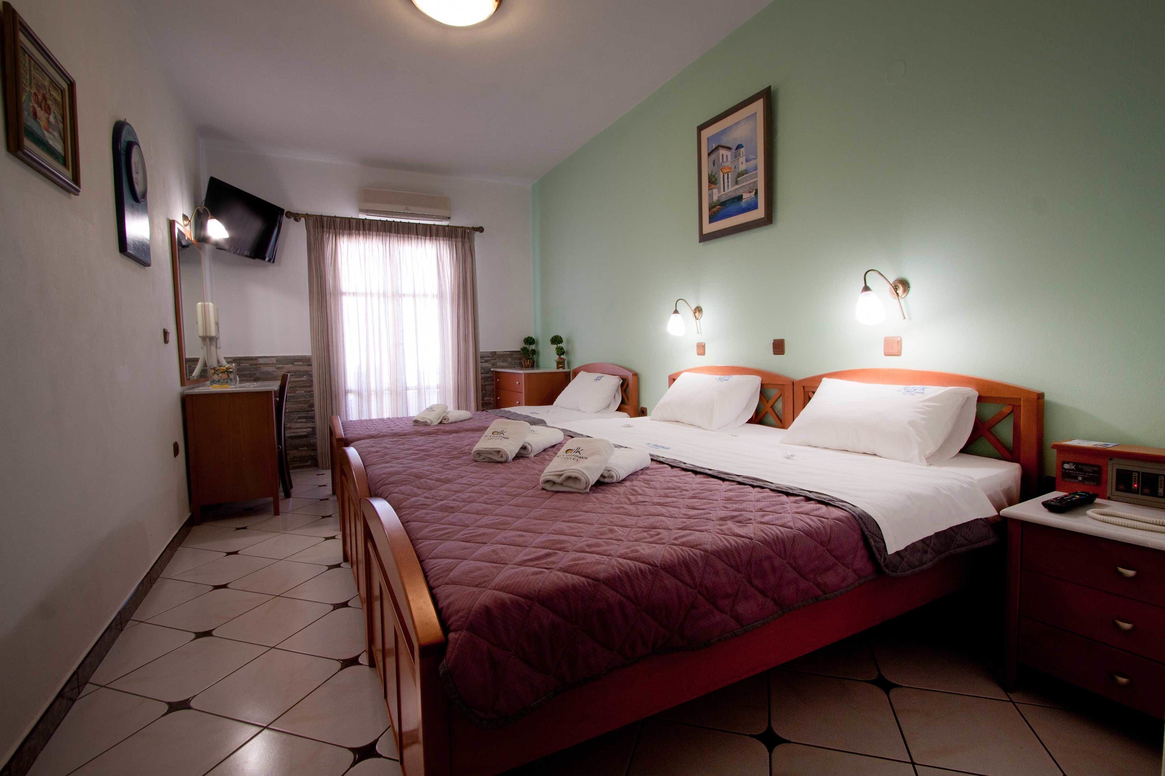 Quarto de hotel com cama, mesas de cabeceira, escrivaninha, cadeira, televisão e janela com cortinas.