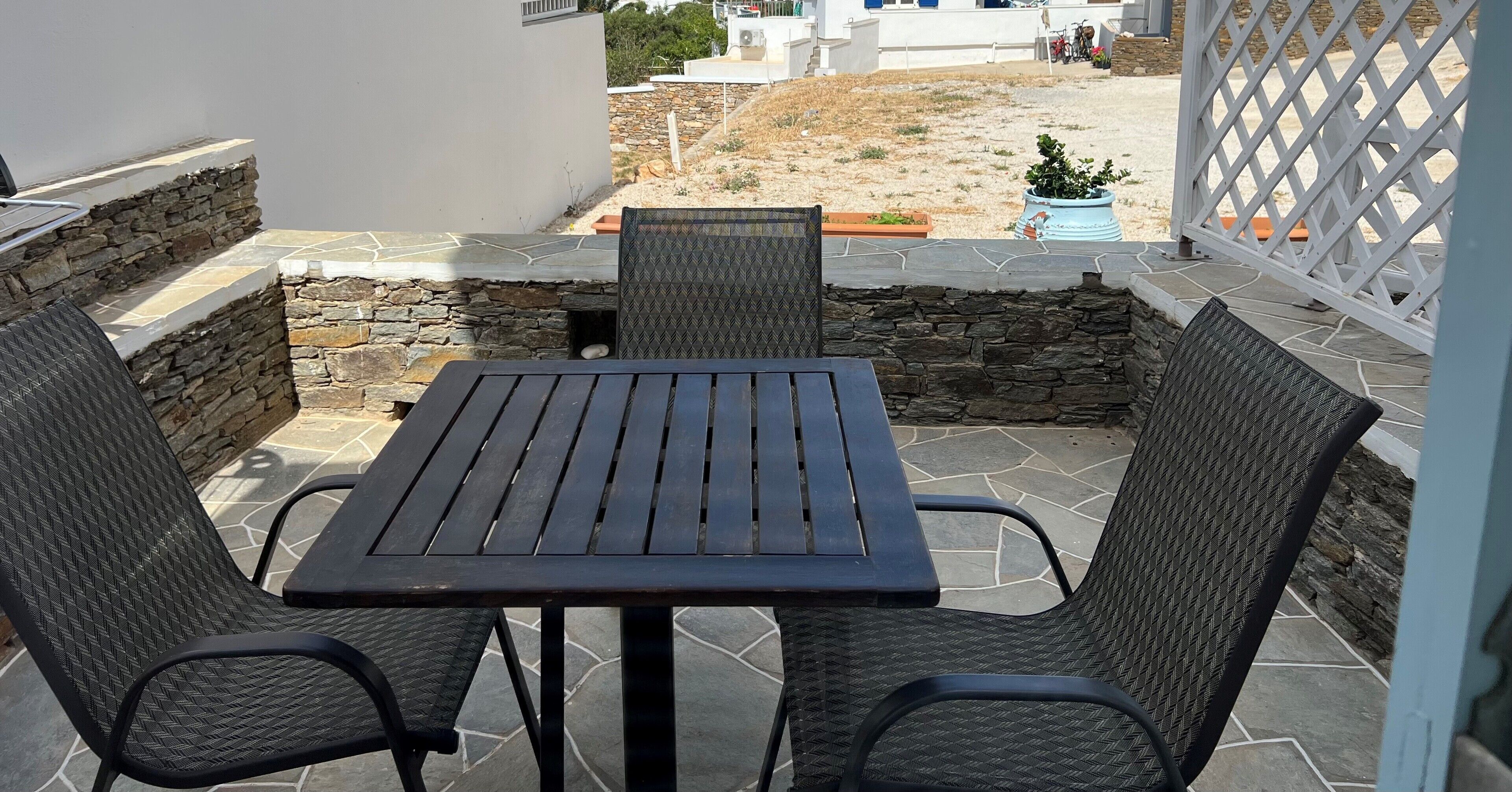 Une terrasse extérieure avec une table et deux chaises, des murs en pierre et une vue sur un quartier résidentiel.