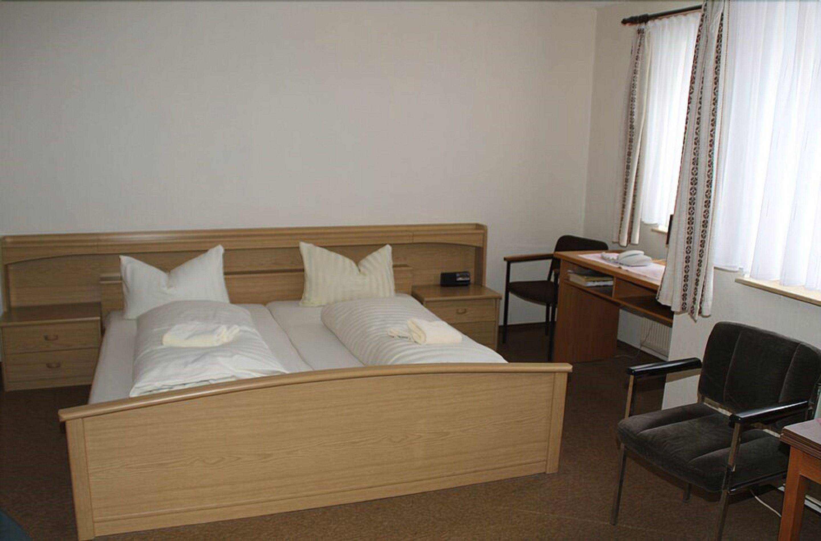 Ein Hotelzimmer mit einem hölzernen Bett, einem Schreibtisch, einem Stuhl und einem Vorhangfenster.