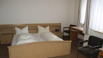 Ein Hotelzimmer mit einem hölzernen Bett, einem Schreibtisch, einem Stuhl und einem Vorhangfenster.