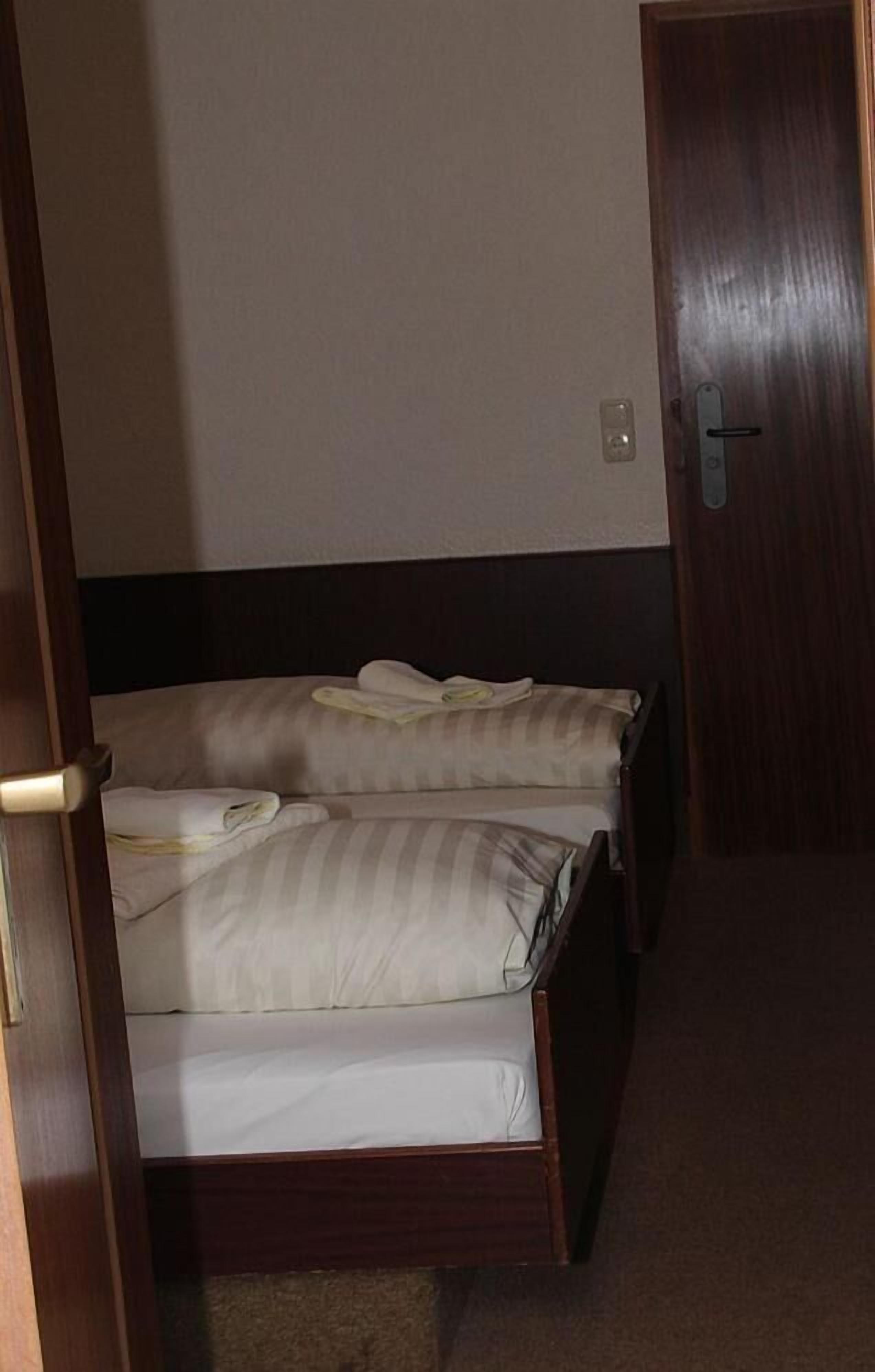 A hotel room with two beds, a wooden headboard, a door, and a light switch on the wall.