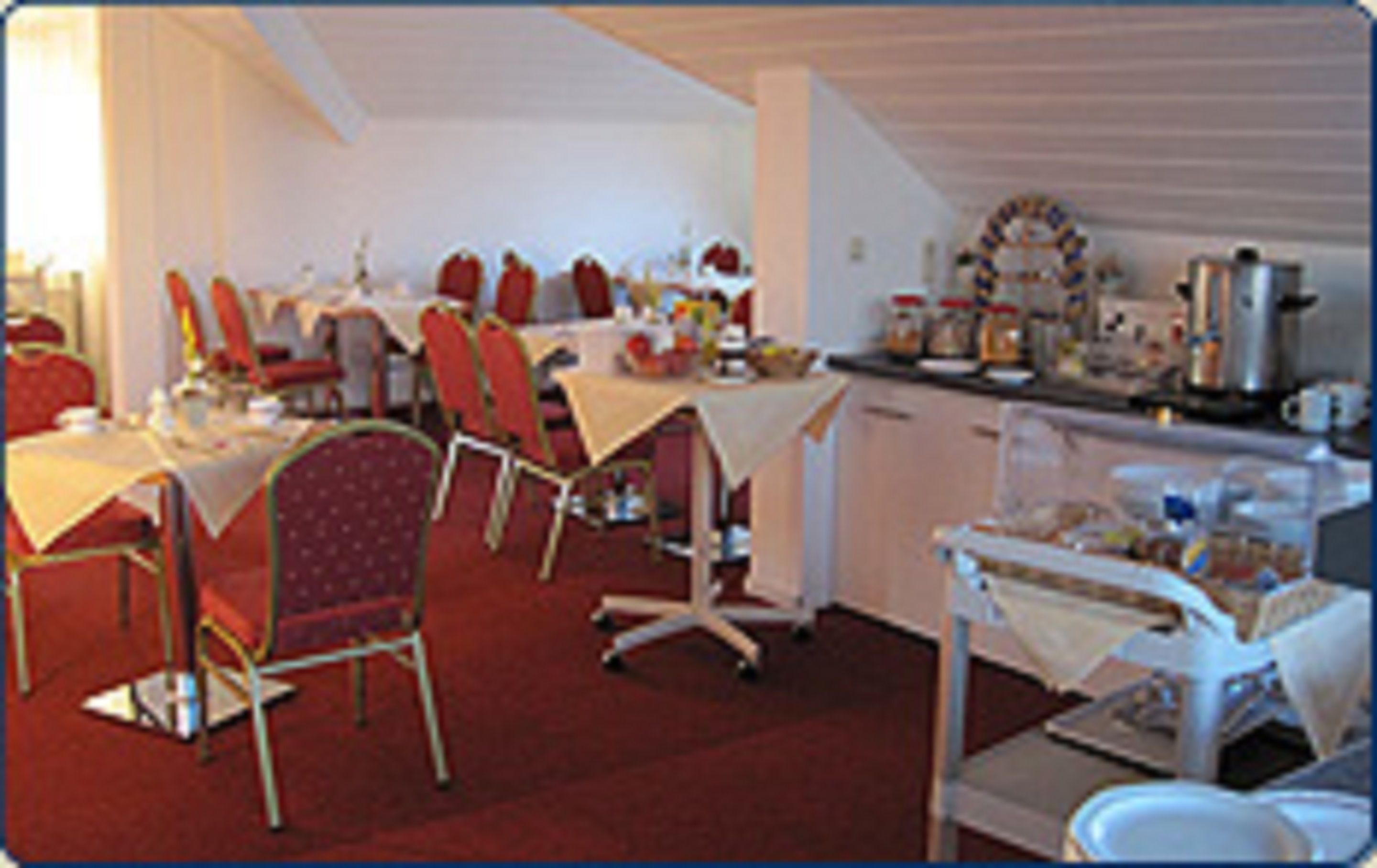 Un espace repas avec plusieurs tables et chaises, un coin cuisine équipé d’appareils électroménagers et un plafond blanc.