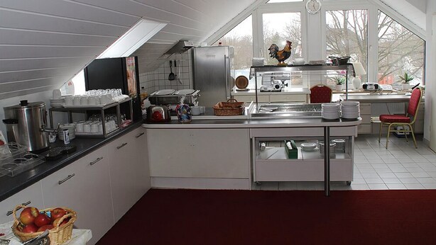 A modern kitchen with white cabinets, a red rug, and a large window with a view of trees. - Einfelder Hof (Neumuenster)