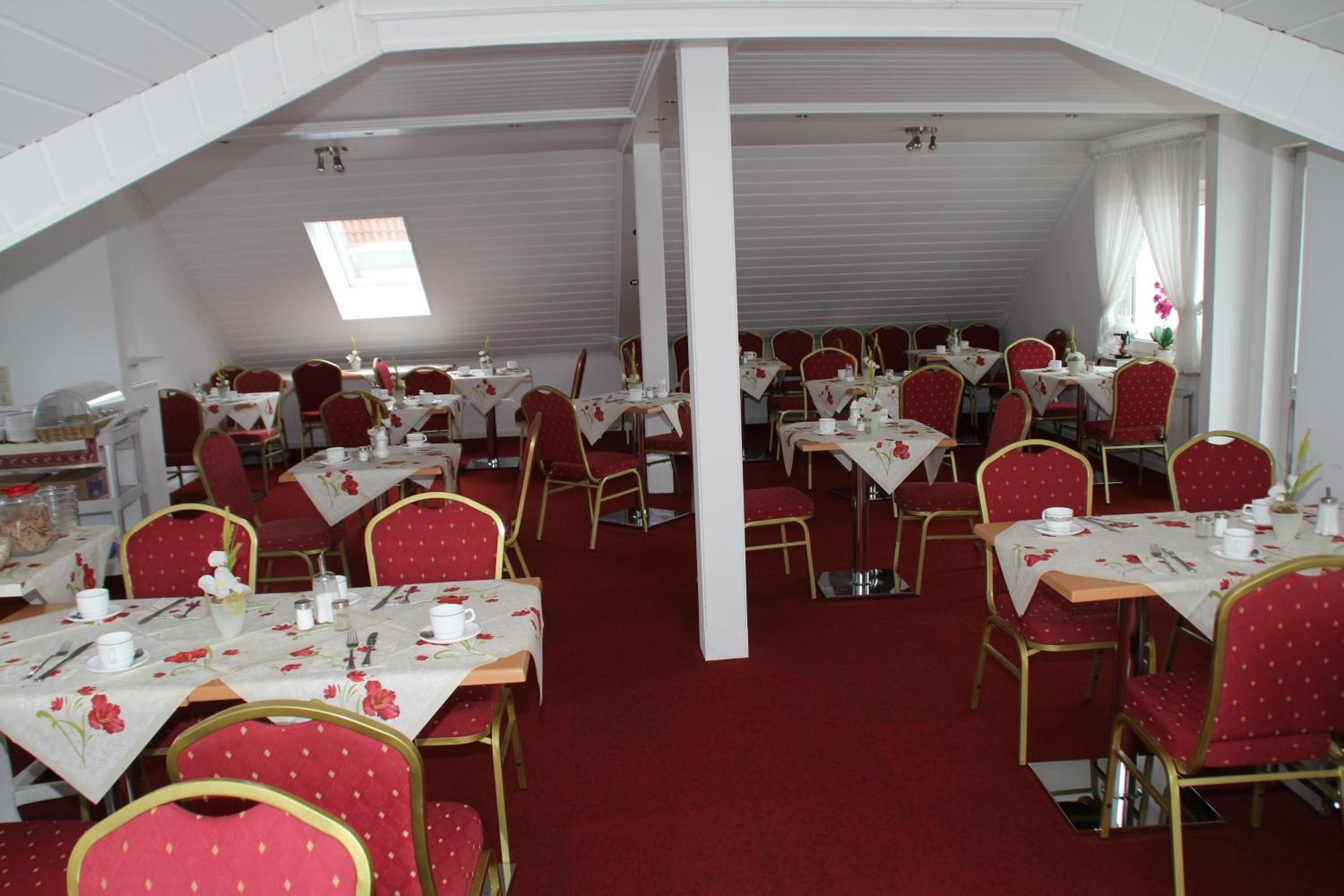 A dining area with red upholstered chairs and tables set with white tablecloths and floral centerpieces.