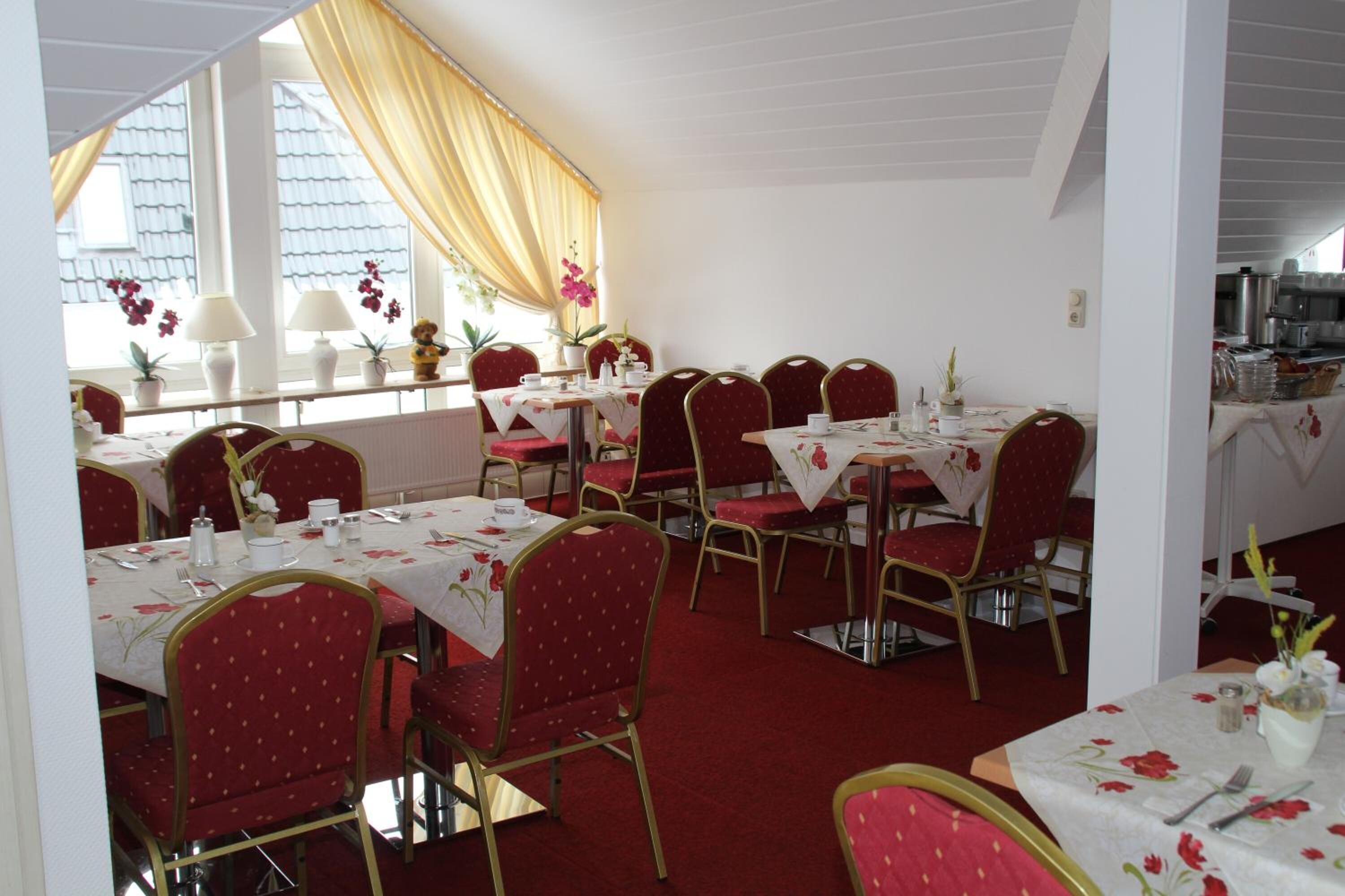 Comedor con mesas dispuestas para el servicio, sillas tapizadas en rojo y vistas al exterior a través de amplias ventanas.