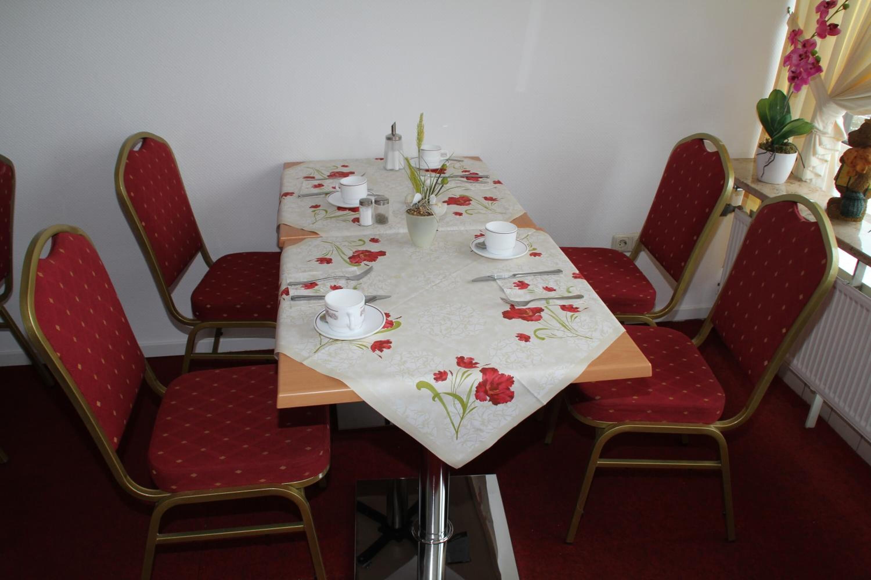 Una mesa de comedor con mantel floreado, rodeada de sillas tapizadas en rojo con marcos dorados.