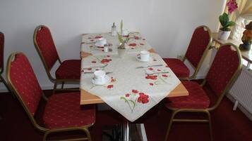 Une table à manger recouverte d’une nappe à motifs floraux, entourée de chaises à revêtement rouge et à cadre doré.