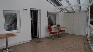 A room with a small table and two chairs, a door, and a window with a curtain. - Einfelder Hof (Neumuenster)