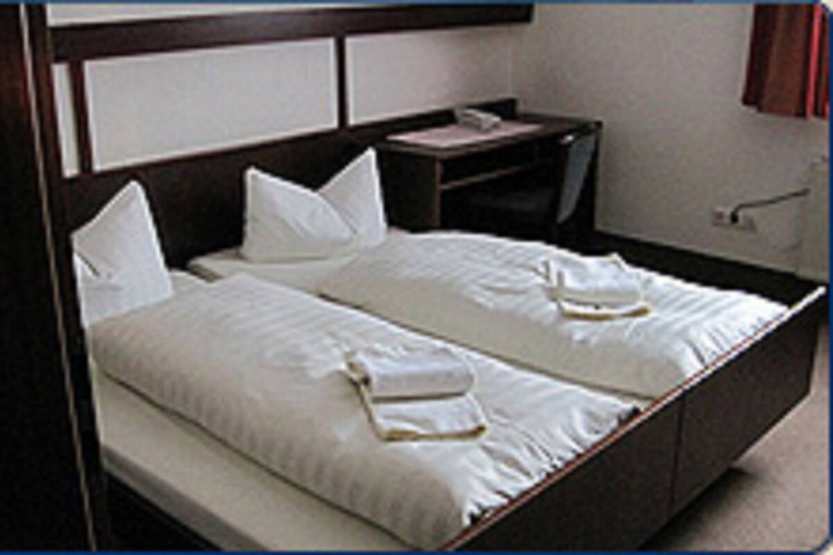 A double bed with white linens and pillows, a bedside table, and a nightstand.