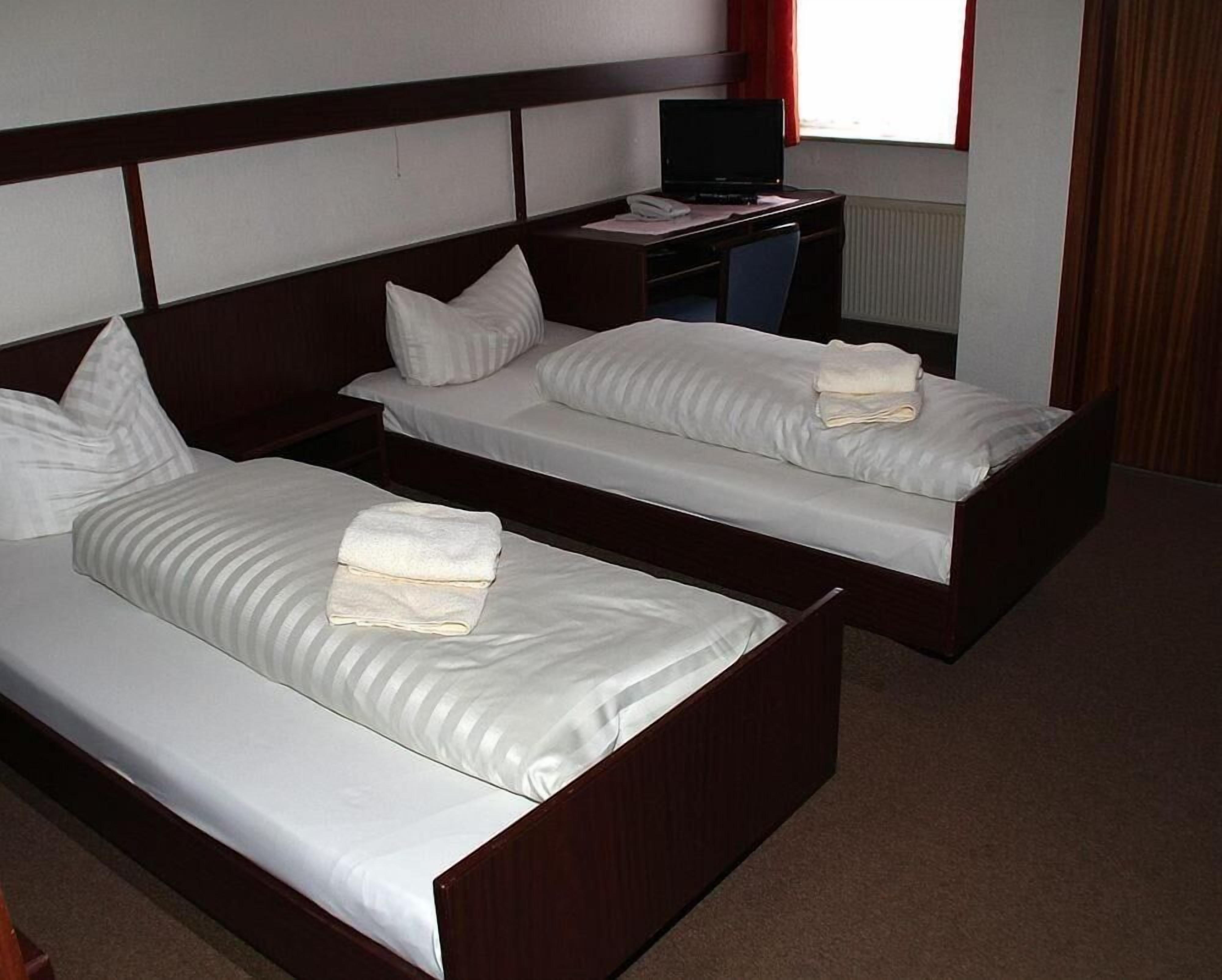 A hotel room with two single beds, a desk with a computer, and a window with curtains.