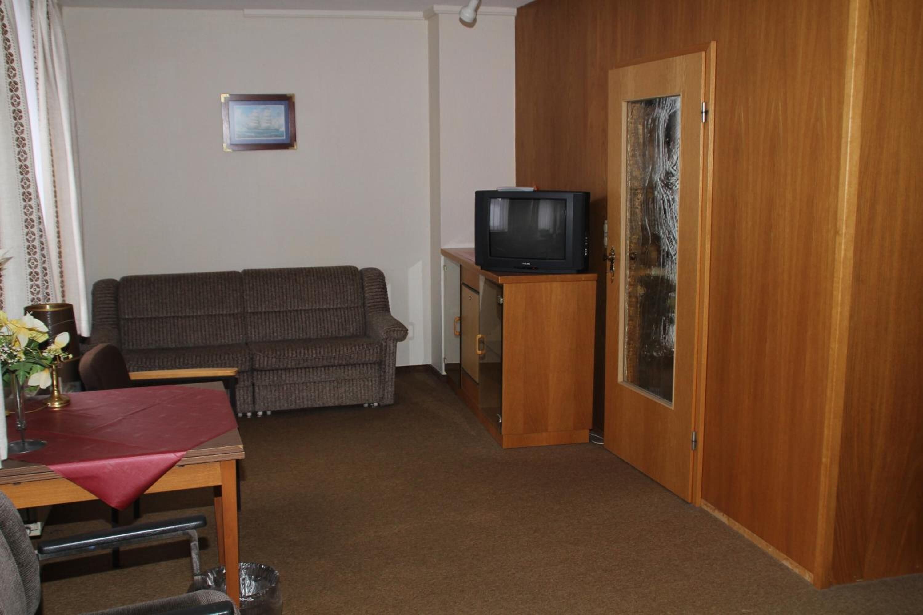 Een woonkamer met een bank, een televisie op een houten dressoir en een deur met een ruit.