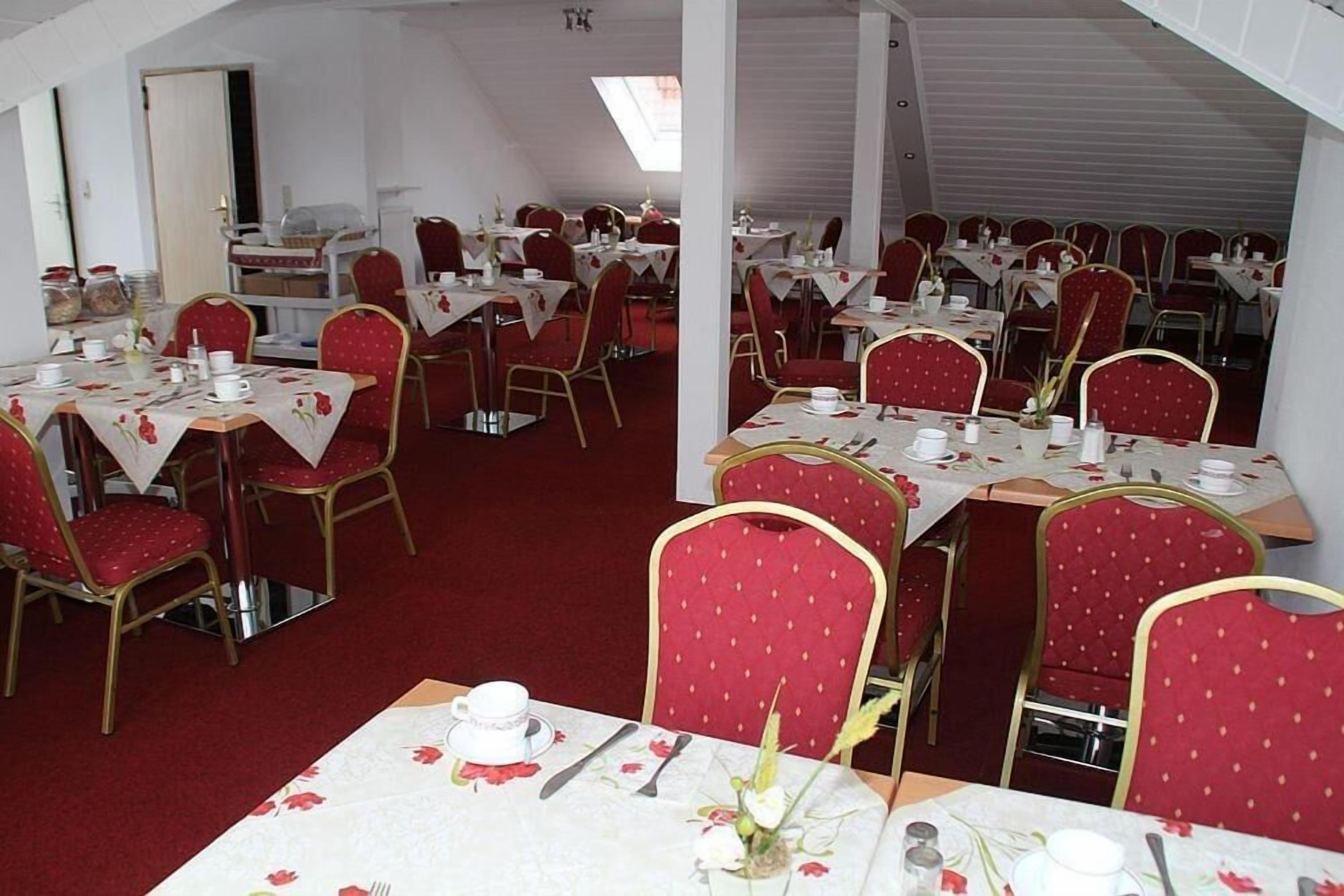 Uma sala de jantar com várias mesas e cadeiras estofadas em vermelho, disposta em um espaço amplo.