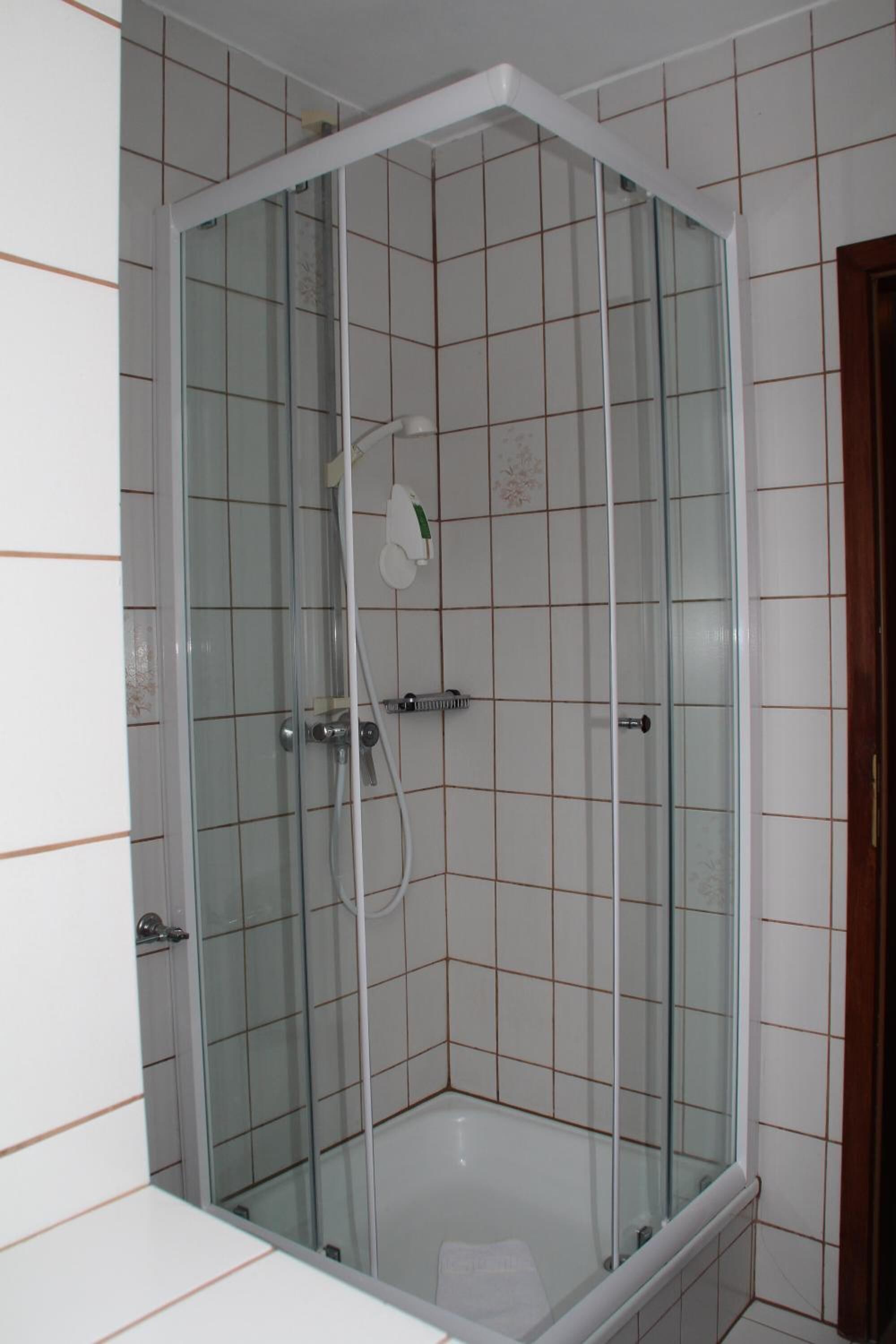 A glass-enclosed shower stall with a white tiled wall and a door.