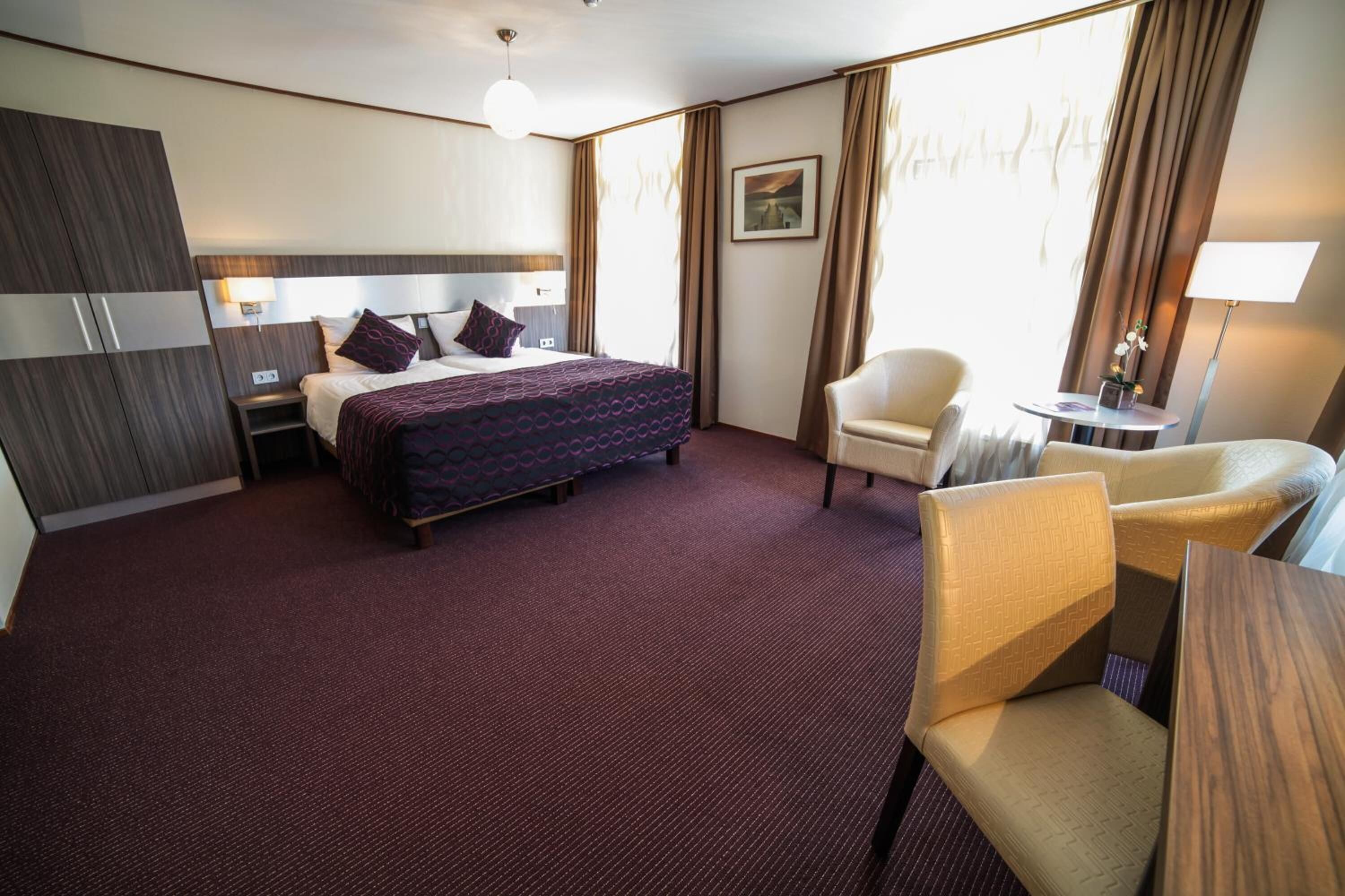 A hotel room with a large bed, a chair, a desk, and a nightstand.