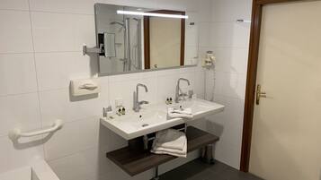 A modern bathroom with a white sink, two faucets, a mirror, and a towel rack.
