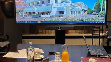 Ein Hotelzimmer mit einem großen Bildschirm, der die Hotelwebsite zeigt, einem Holztisch mit einer Obstschale, einem Glas Orangensaft und einem Laptop.