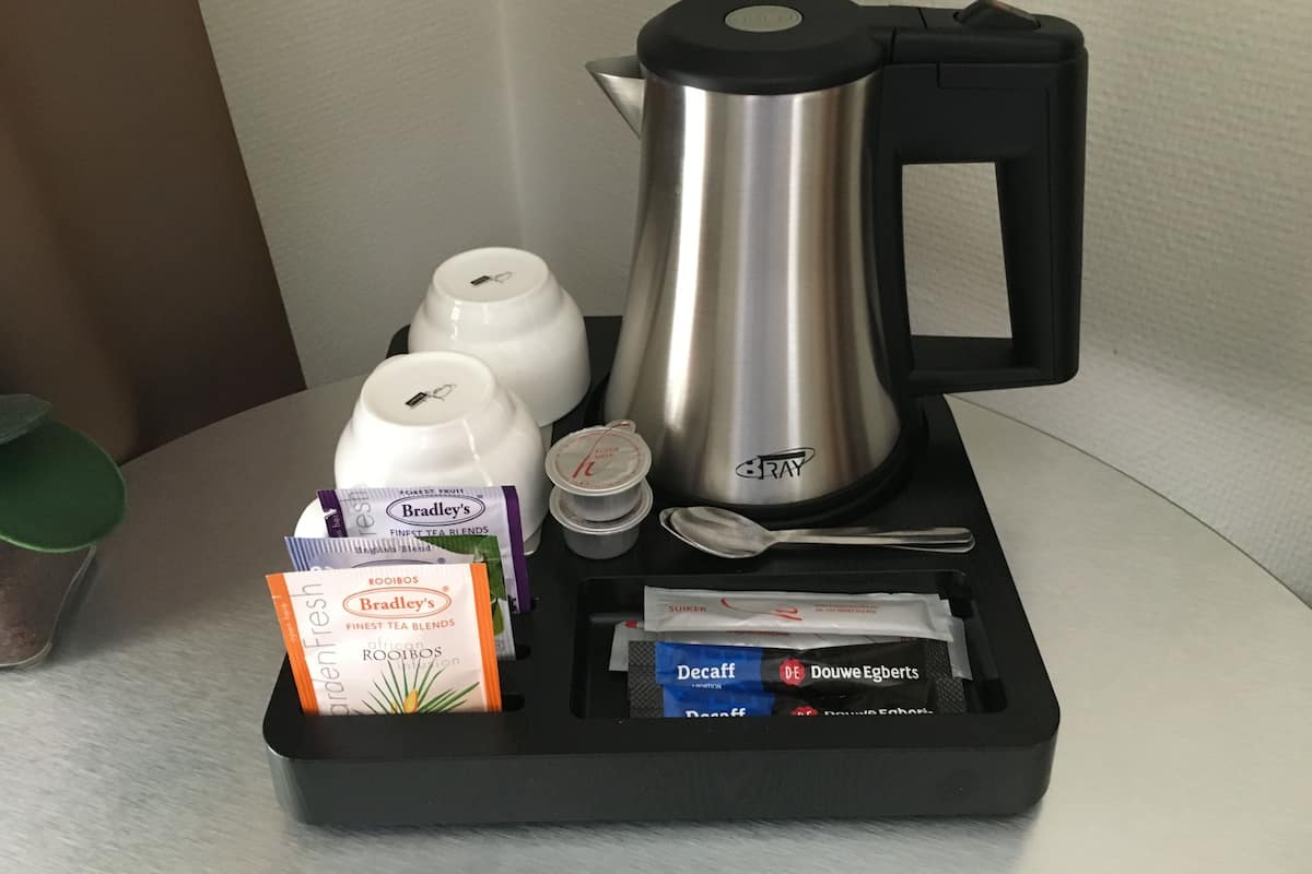 A tray with a silver coffee pot, two white teapots, a spoon, and packets of tea blends.