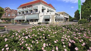 A hotel with a red roof and striped awnings, surrounded by a garden of pink flowers. - Hotel Faber (Hoogezand)