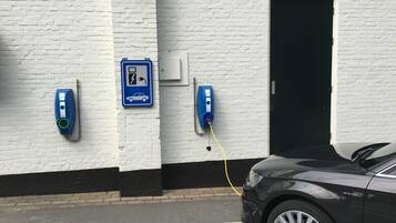 Un’area di parcheggio con stazioni di ricarica per veicoli elettrici, un muro in mattoni bianchi e un’auto nera parcheggiata.