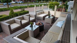 An outdoor patio area with wicker furniture, including sofas and chairs, arranged around a central fire feature. - Hotel Faber (Hoogezand)