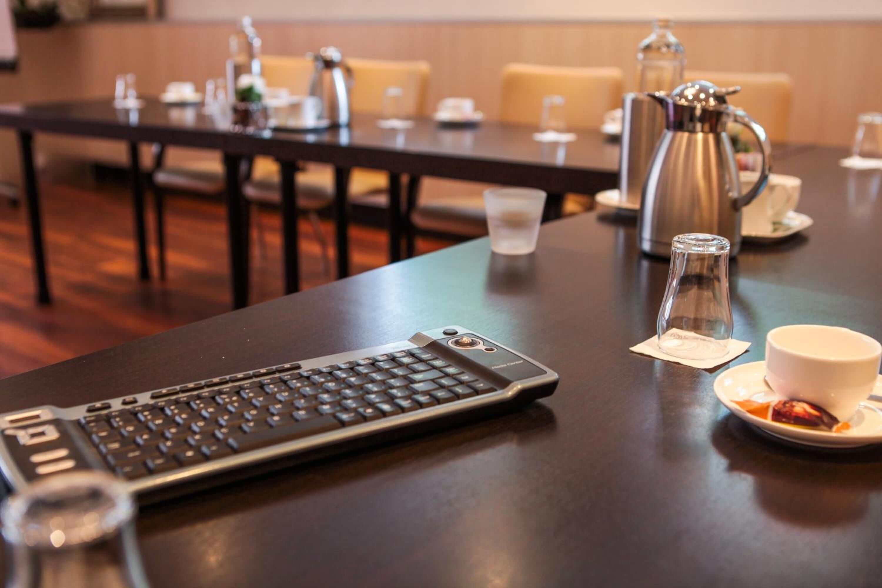 Ein Konferenztisch mit einem Laptop, einer Kaffeemaschine und einer Kaffeetasse.