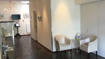 Een modern interieur met een receptiebalie, twee leren fauteuils, een flatscreen televisie en een donker vloerkleed.