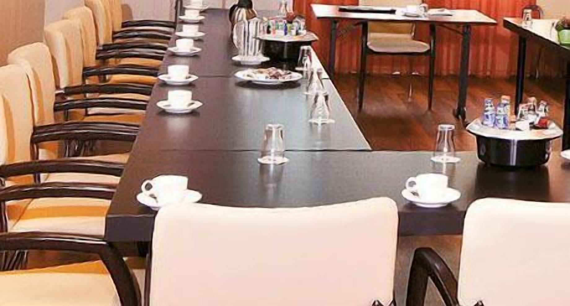 A long dining table set with white plates, cups, and cutlery, surrounded by chairs.