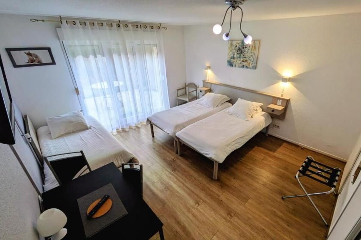 Une chambre avec deux lits, un bureau, une chaise, une petite table et une fenêtre avec des rideaux.