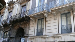 A historic building with ornate iron balconies, a large arched entrance, and a storefront with a sign. - Elios Rooms (Catania)