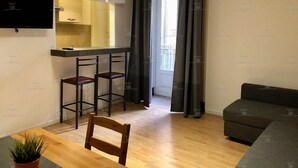 A compact living space with a kitchenette, a dining area with a chair and table, a sofa, and a large window with curtains. - Elios Rooms (Catania)
