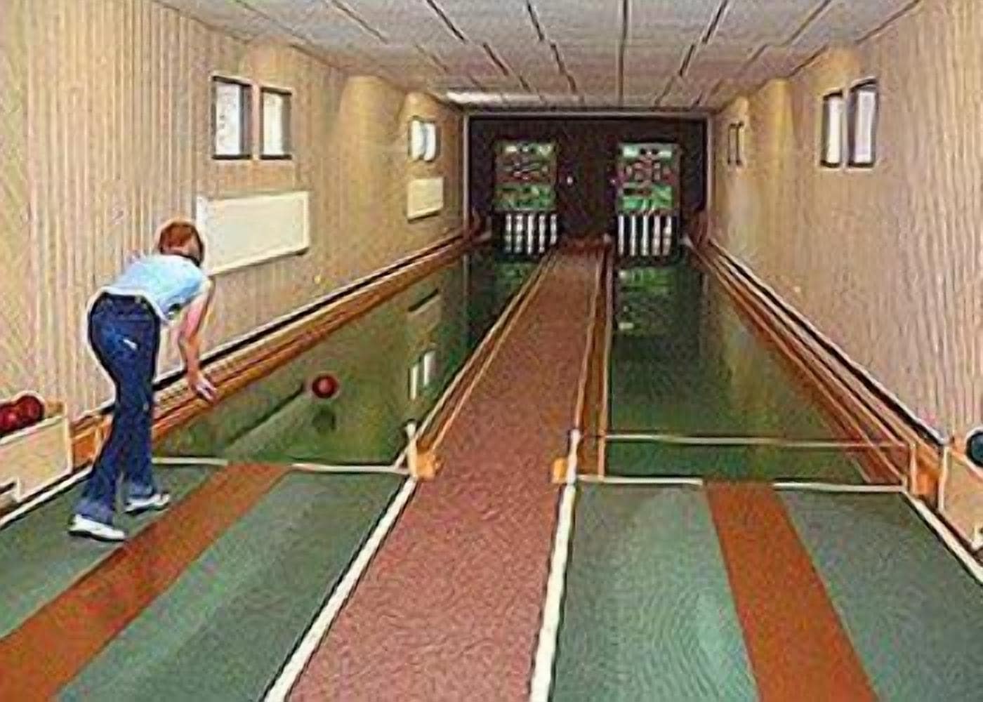 A bowling alley with lanes, a person bowling, and a green carpeted floor.