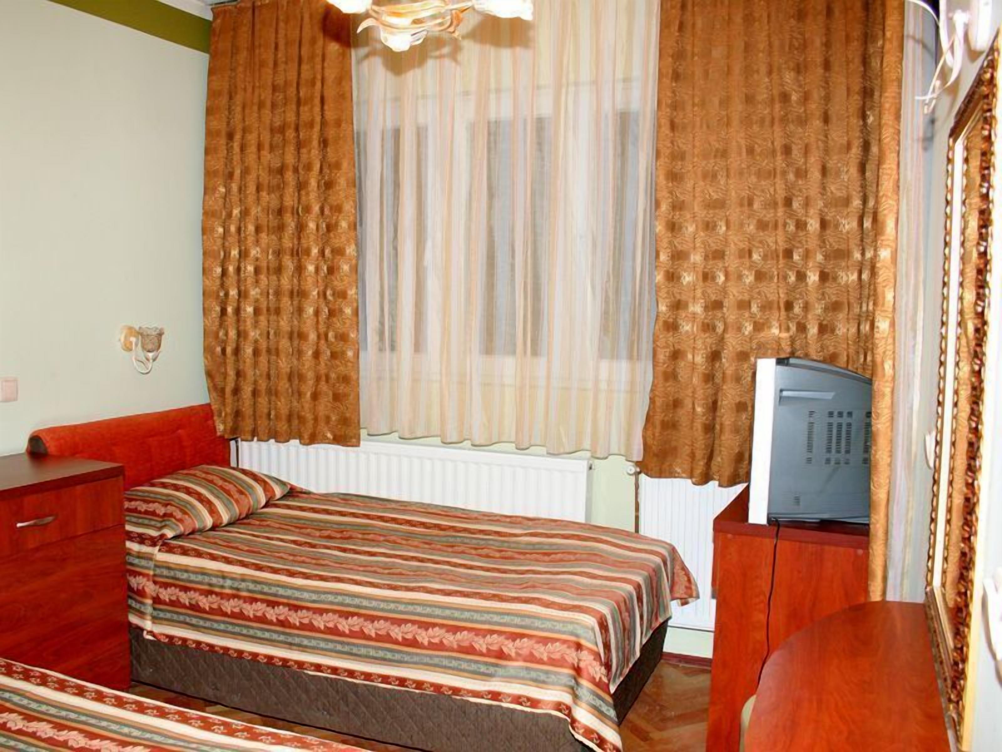 Ein Schlafzimmer mit einem Bett, einer Holzkommode, einem Fernseher auf einem Standfuß und einem Fenster mit Vorhängen.
