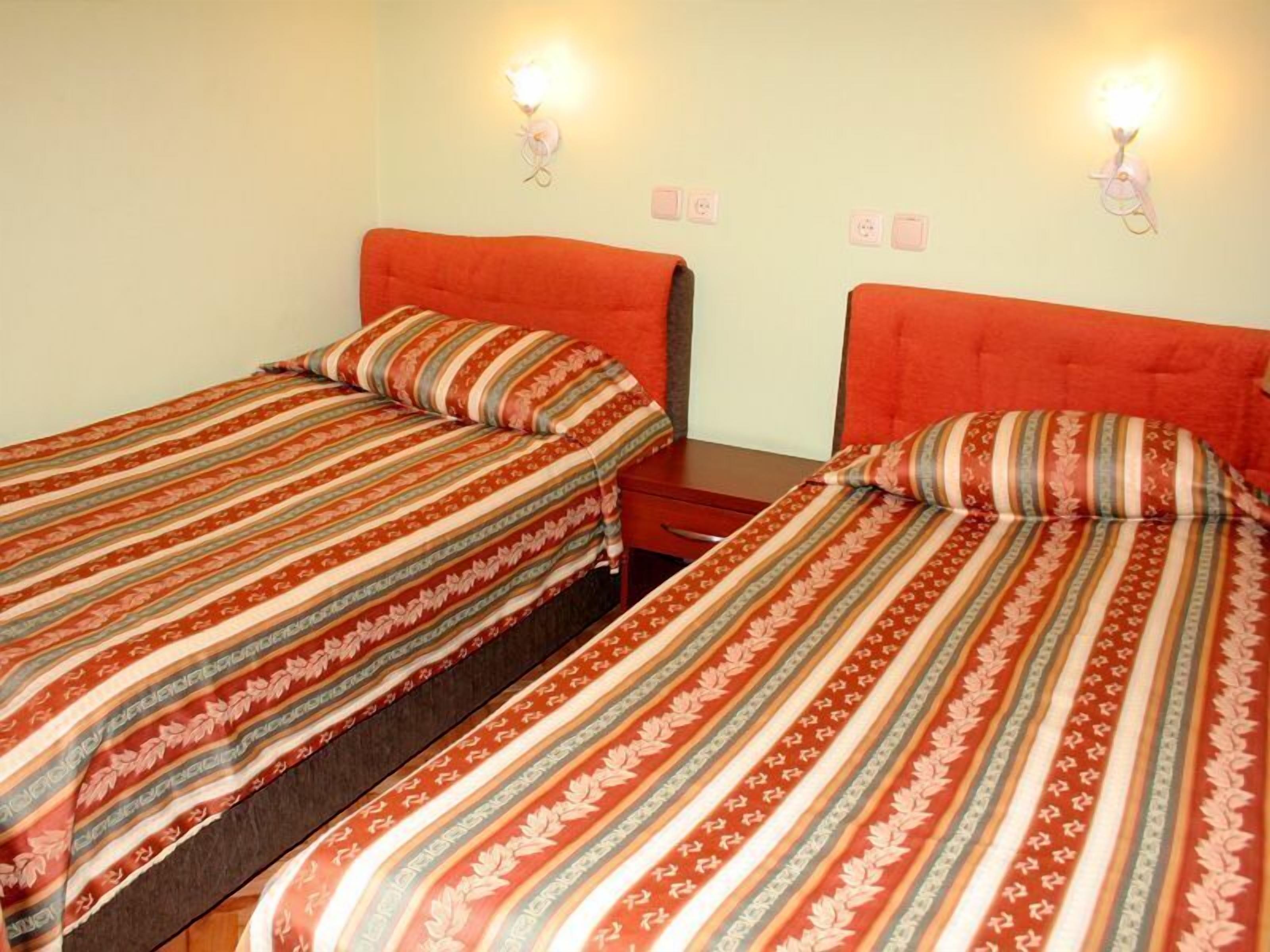Una stanza con due letti singoli, ognuno con copripiumino a righe e cuscini coordinati. Sopra ogni letto sono presenti applique.