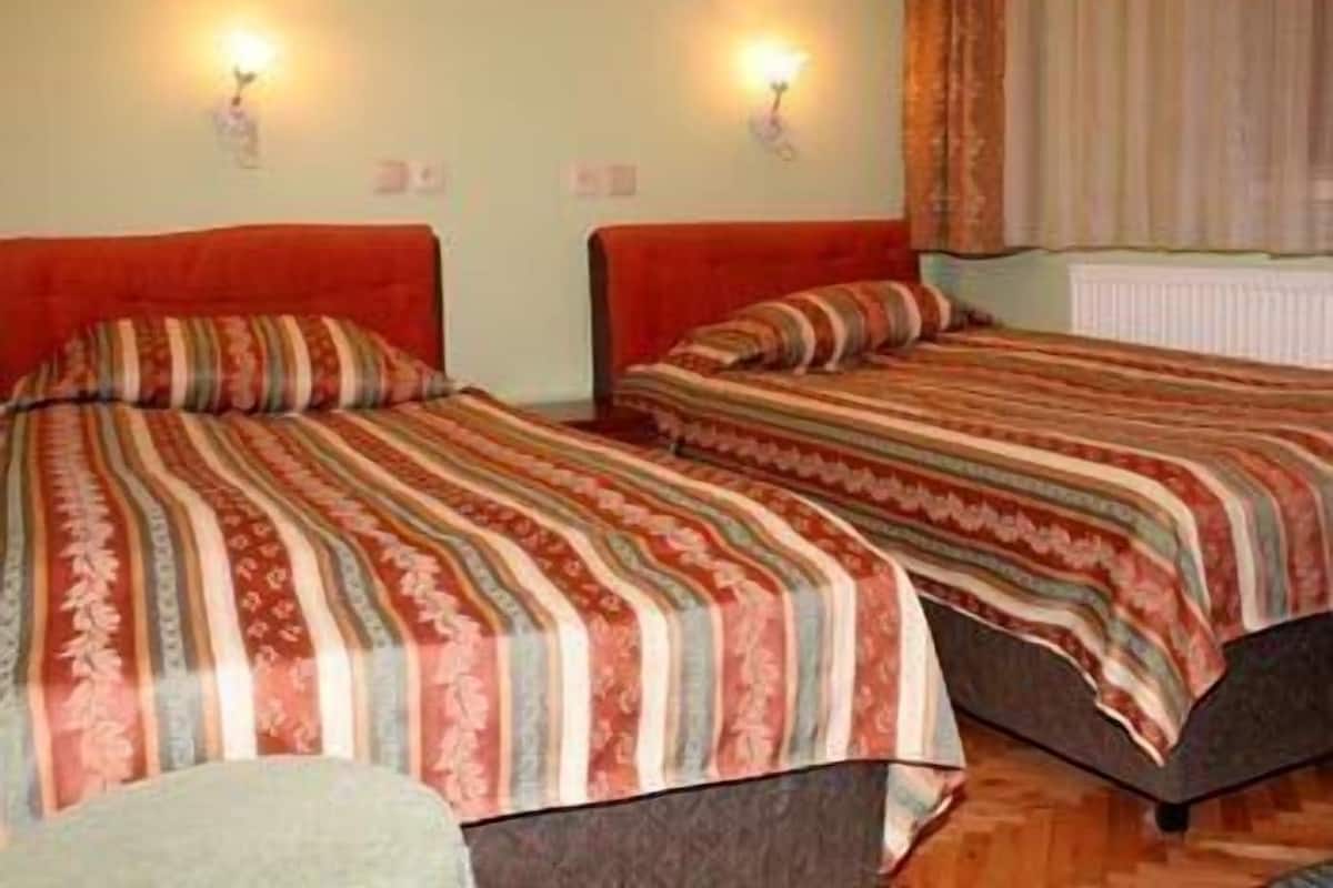 A hotel room with two beds, each with a striped bedspread and two wall-mounted lamps.
