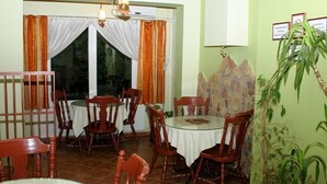 Een eetruimte met een ronde tafel en stoelen, een kroonluchter, gordijnen en een stenen muur met ingelijste certificaten.