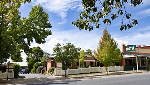 A motel with a white picket fence, a signboard, and a clear blue sky. - Beechworth Carriage Motor Inn (Beechworth)
