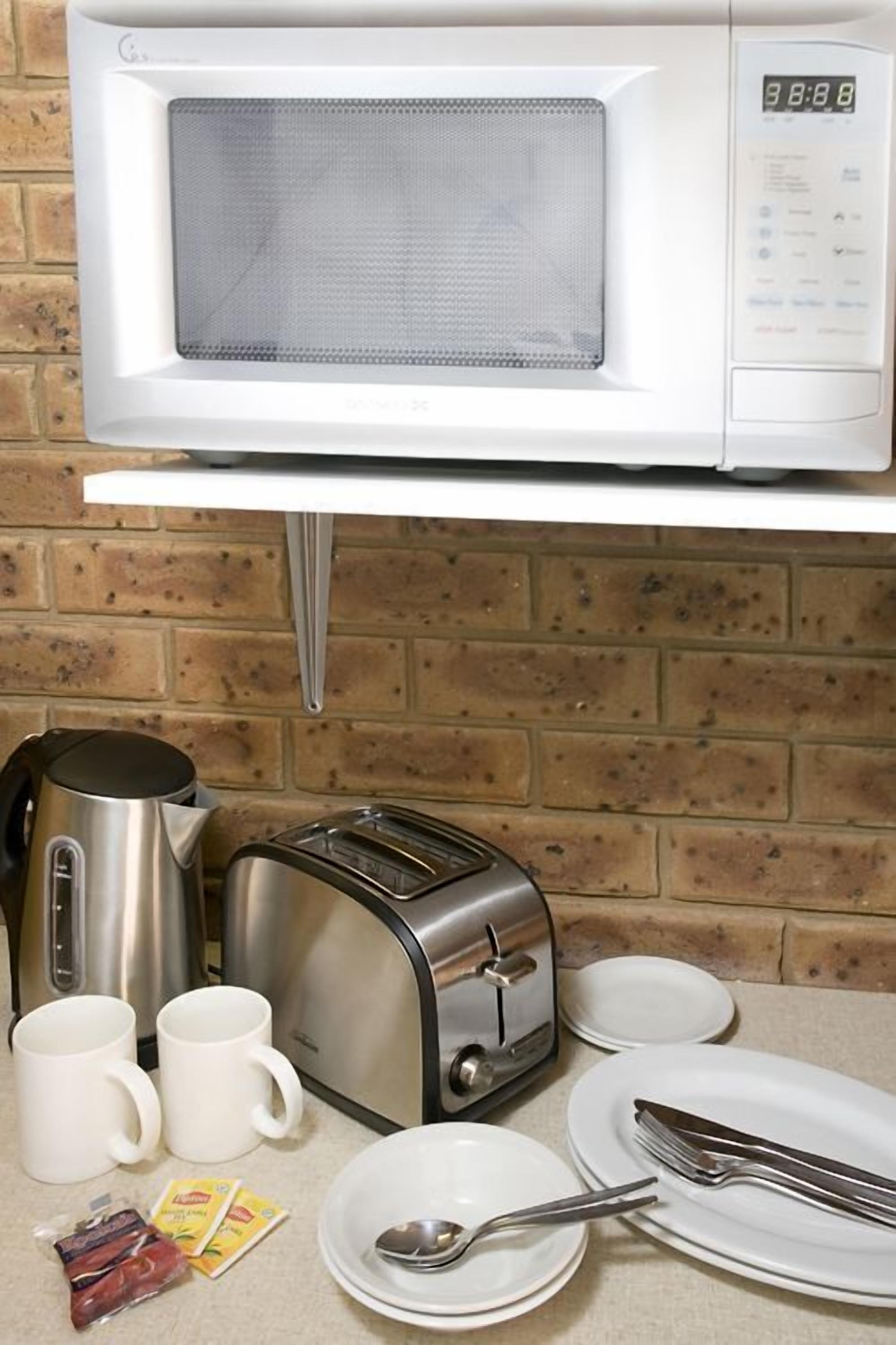 A kitchen with a microwave, toaster, kettle, and table set with plates, cups, and utensils.