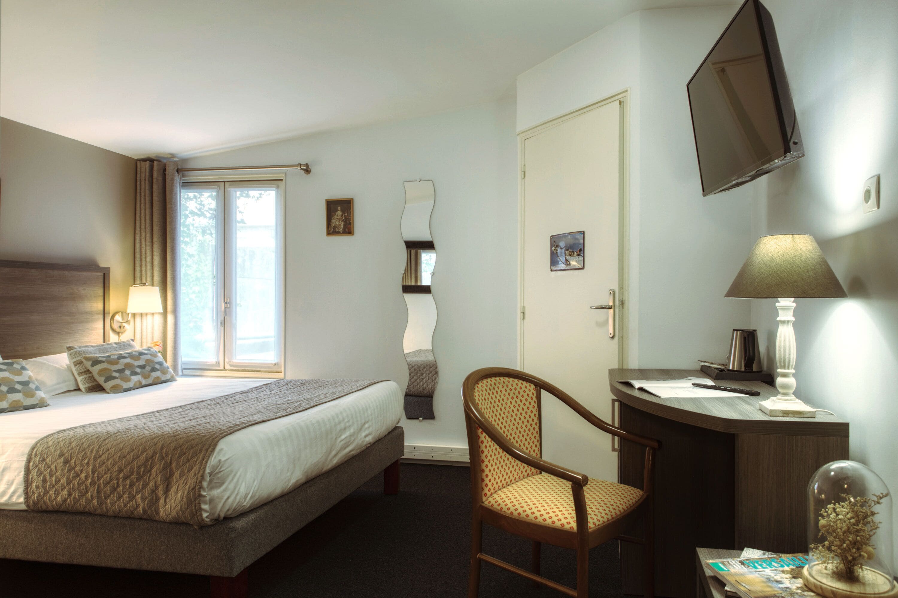 Een hotelkamer met een bed, bureau, stoel, televisie en raam.