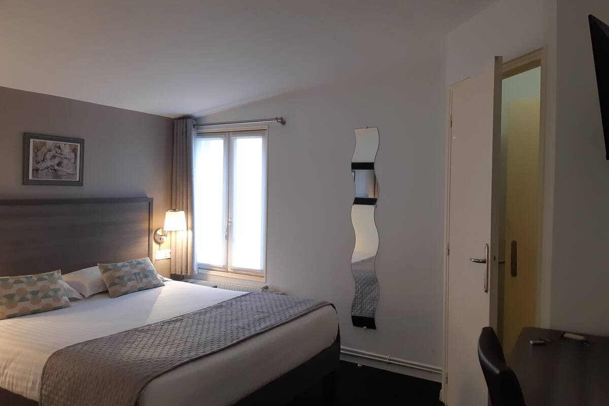 Habitación de hotel con cama, lámpara de noche, ventana y puerta.