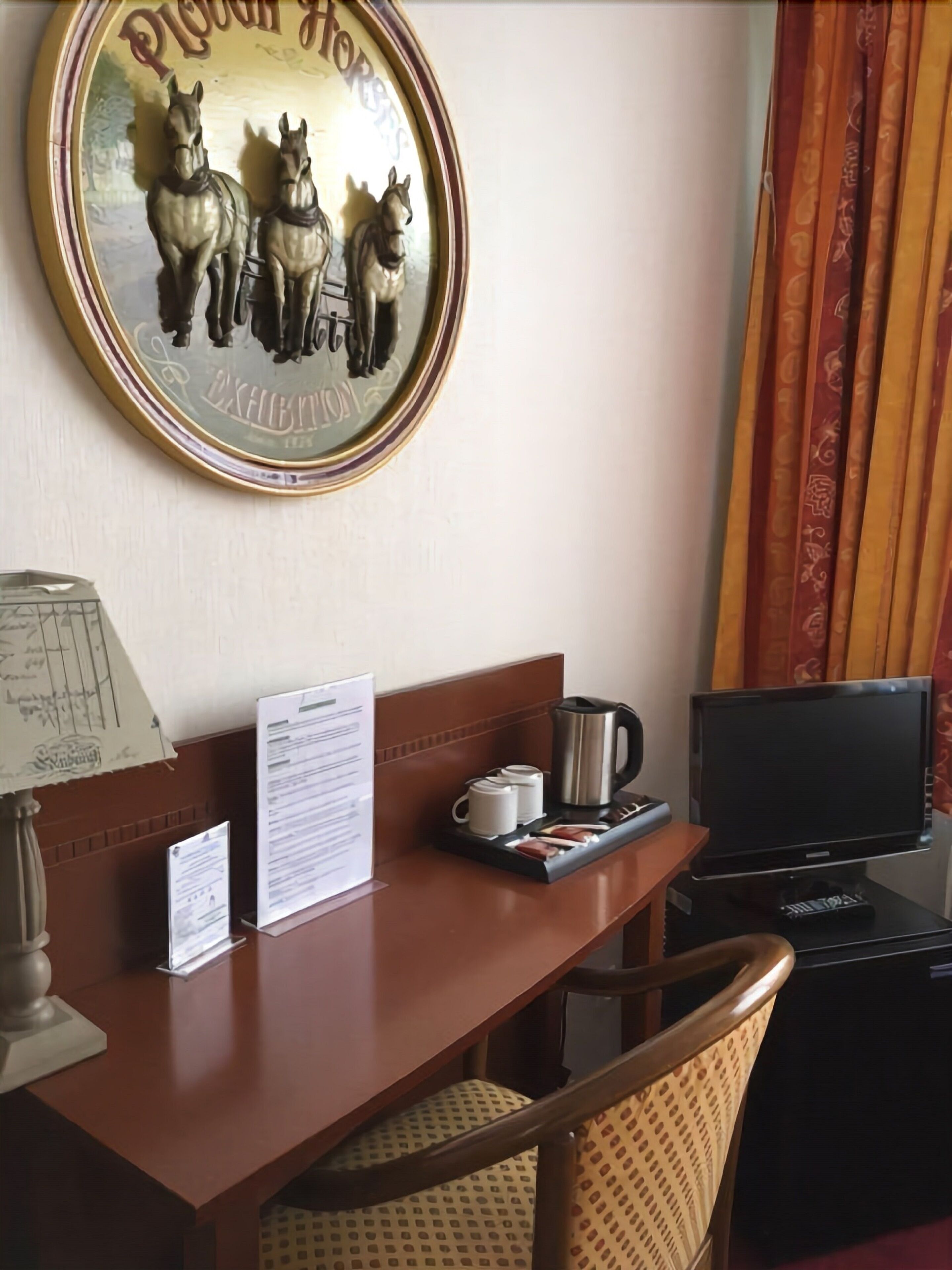Een hotelkamer met een houten bureau, een televisie, een koffiezetapparaat en een decoratie van paarden.