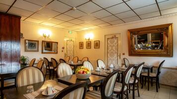 A dining area with multiple tables and chairs, a fruit bowl on one table, and framed pictures on the walls.