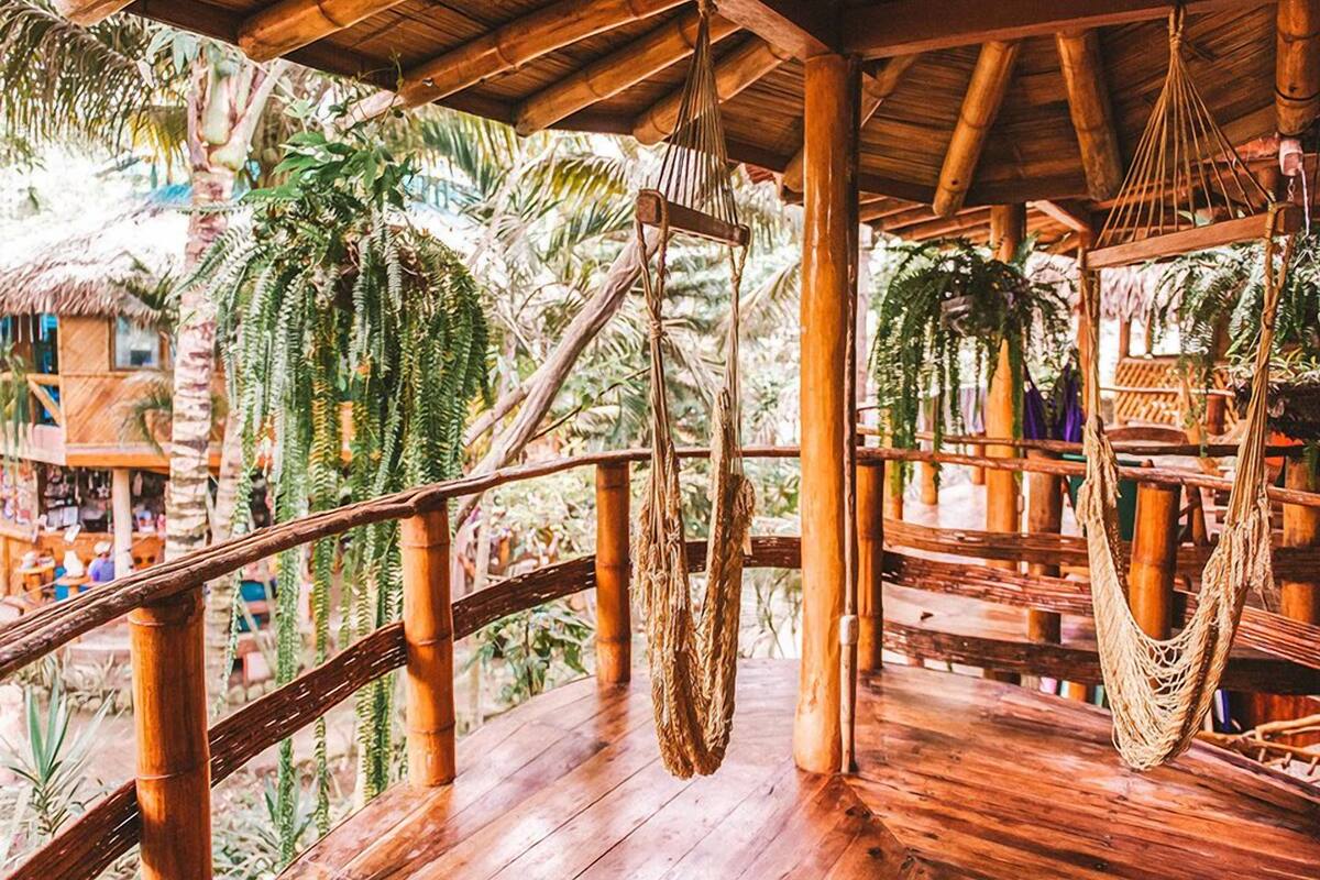 A wooden deck with a thatched roof, bamboo railings, and hanging hammocks.